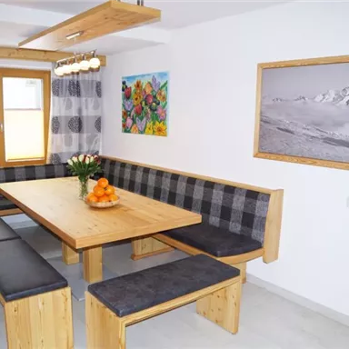 Ein einladender Essbereich mit einem großen Holztisch und gemütlichen Bänken. Die Wände sind mit Farbkunswerken und einem Schwarz-Weiß-Foto dekoriert.