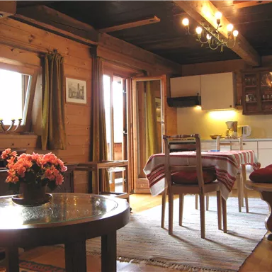 Ein gemütlicher Wohnraum mit Holzwänden, einem Tisch und Stühlen. Das Zimmer hat Fenster mit Vorhängen und eine gemütliche Atmosphäre.