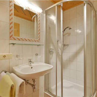 A modern bathroom with a shower cabin and a sink. The walls are tiled with white tiles, and there is a mirror above the sink.