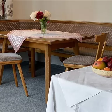 Ein gemütlicher Essbereich mit einem Holztisch und Stühlen. Auf dem Tisch steht eine Vase mit Blumen und eine Schüssel mit frischem Obst.