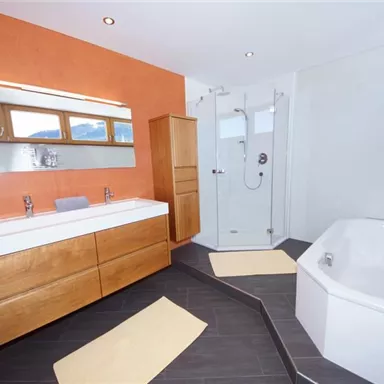 Ein modernes Badezimmer mit Holzschränken und einer stylischen Dusche. Die orangefarbene Wand sorgt für eine warme Atmosphäre.