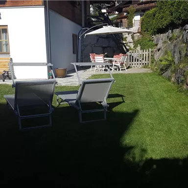 A quiet garden with loungers and a sun umbrella. In the background, there is a cozy seating area, and there are rocky sections.