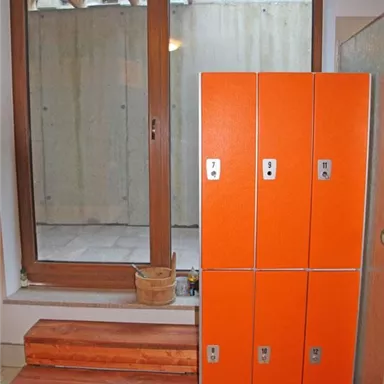 A room with a large window through which daylight streams. On the right, there are orange lockers, and on the left, wooden steps are visible.