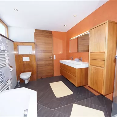 Ein modernes Badezimmer mit Holz- und weißen Möbeln. Es gibt eine Dusche, eine Badewanne und große Fenster, die viel Licht hereinlassen.