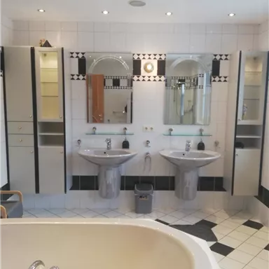 A modern bathroom with a bathtub and two sinks. The walls are tiled in light colors and equipped with stylish mirrors and cabinets.