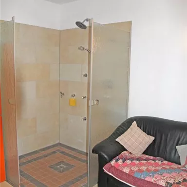 A bathroom with a modern glass shower and a dark sofa. The floor is tiled and the walls are painted light.