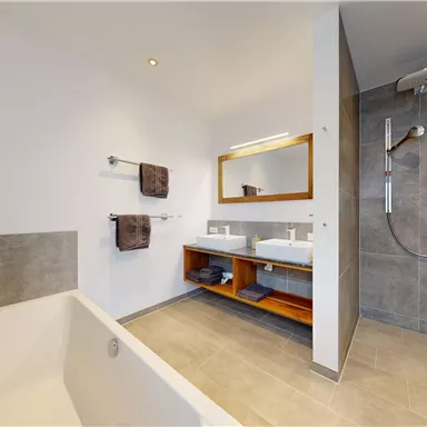 A modern bathroom with a bathtub and a separate shower. The space is tastefully decorated with towels and a large mirror.