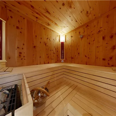 A modern wooden sauna with bright walls and benches. The room has a sauna stove and cozy lighting.