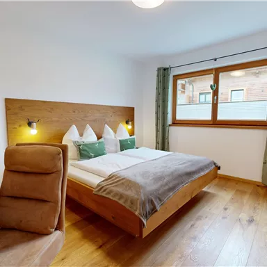 A modern bedroom with a double bed and wooden details. The room is bright and welcoming, with a desk and a television.
