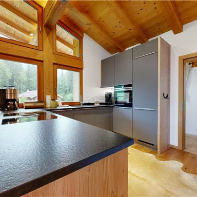 A modern kitchen with large windows and wood-paneled ceilings. The room has a clean, minimalist design and plenty of daylight.