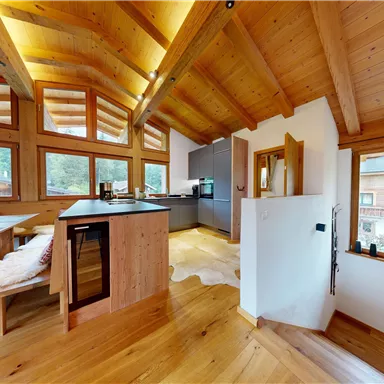 A modern kitchen with wooden ceilings and large windows. The dining area is bright and inviting.
