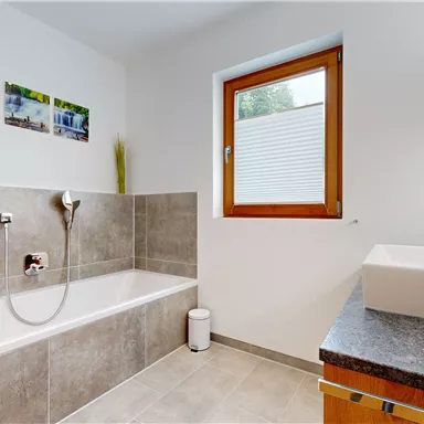 A modern bathroom with a bathtub and a large window. On the wall, there are pictures of waterfalls.
