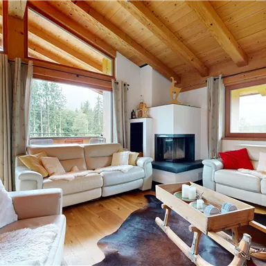 A cozy living room with wooden ceilings and large windows. Two bright sofas and a table in an inviting, modern style.