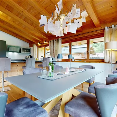 A modern dining room with a wooden ceiling and large windows. The table is elegantly set and surrounded by stylish chairs.