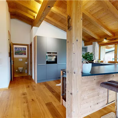 A modern kitchen with a wooden ceiling and elegant furniture. The room is bright and inviting with large windows that let natural light in.