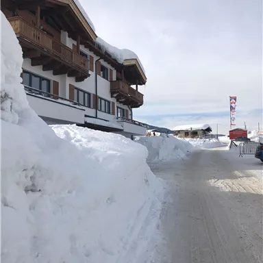 Ein schneebedeckter Weg neben einem Gebäude in den Bergen. Der Himmel ist klar und die Atmosphäre ist winterlich.