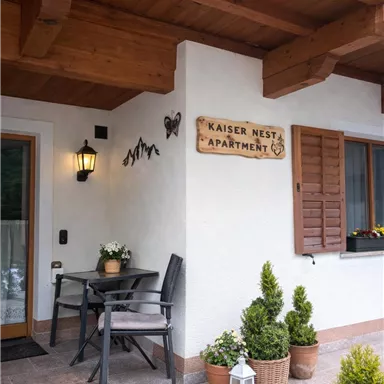 The entrance area of an apartment called "Kaiser Nest." There is a table with chairs and well-kept plants in pots.