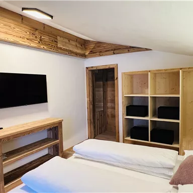 Ein modernes Schlafzimmer mit Holzverkleidung und einem Fernseher an der Wand. Es gibt ein gemütliches Bett und Regale mit dunkelblauen Boxen.
