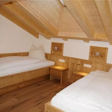 Ein gemütliches Schlafzimmer mit holzverkleideten Wänden und zwei Betten. Es gibt kleine Nachttische und ein warmes, einladendes Ambiente.