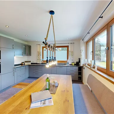 Bright, modern kitchen with a long wooden table and large windows that let in plenty of natural light. An inviting space with elegant gray cabinets and a view of the garden.