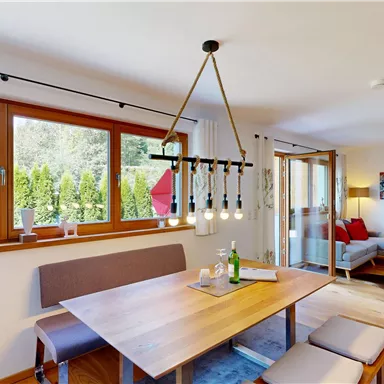 A modern living room with a wooden dining area. Large windows bring in plenty of light and offer a view of the garden.