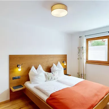 A cozy bedroom with a double bed and wooden details. The windows let in plenty of daylight and the orange ceiling adds a warm touch.