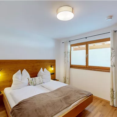 A modern bedroom with a double bed and wooden cladding. Bright walls and a window create a friendly atmosphere.