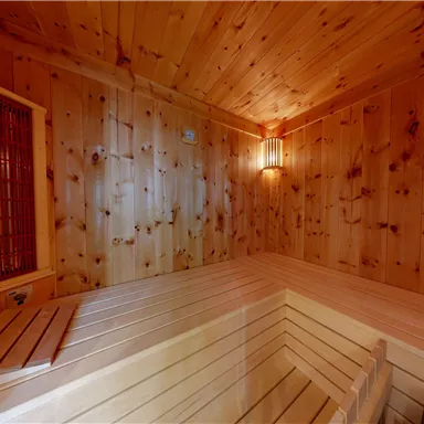 A cozy sauna with wooden paneling and soft lighting. The benches are made of light wood and provide space to relax.