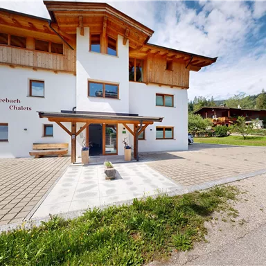 A modern building with a timber and stone frame. In front of the entrance, there is a path and a well-kept garden.