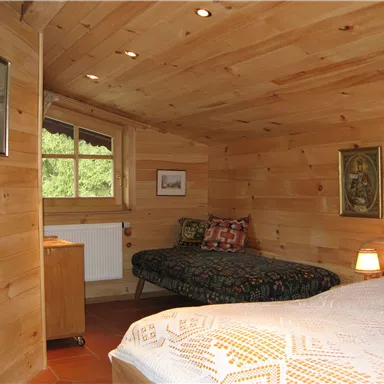 Ein gemütliches Zimmer mit Holzwänden und zwei Betten. Es gibt ein Fenster mit Blick nach draußen und eine kleine Lampe auf dem Nachttisch.