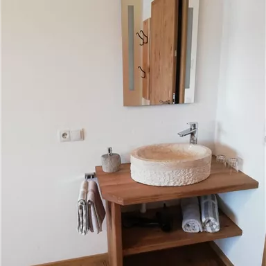 A modern bathroom with an elegant stone sink on a wooden table. In the background, there is a mirror and towels are neatly hung.