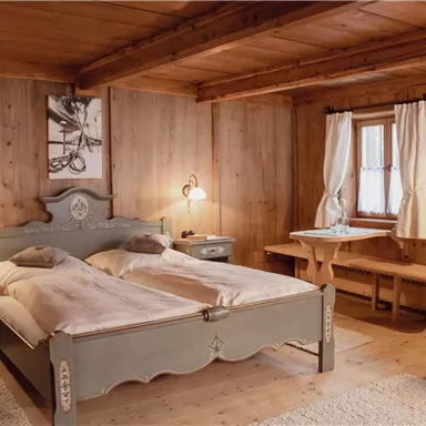 Ein gemütliches Schlafzimmer mit einem großen, komfortablen Bett und holzgetäfelten Wänden. Neben dem Bett stehen ein Nachttisch und ein Tisch mit Stühlen.