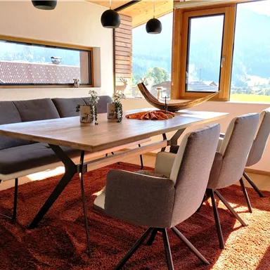 A modernly furnished dining area with a large table and cozy chairs. Through the window, you can see a picturesque mountain landscape.