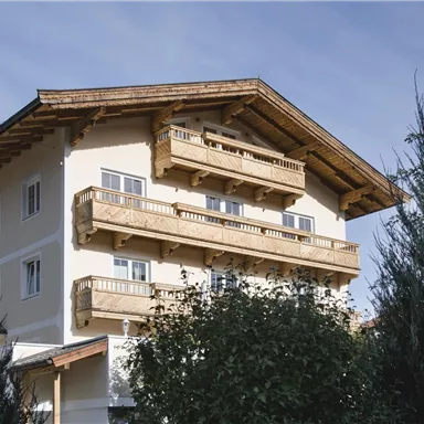 Ein elegantes Gebäude mit einem Holz-Dach und Balkonen. Es ist von grünen Bäumen umgeben und hat einen klaren blauen Himmel im Hintergrund.