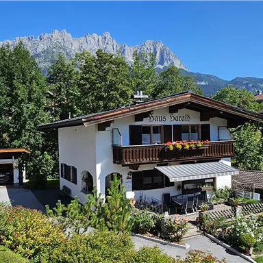 A charming house adorned with flowers in a picturesque landscape. In the background, tall mountains and a clear blue sky can be seen.