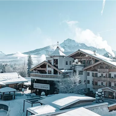 Eine malerische Winterlandschaft mit schneebedeckten Bergen und einem charmanten Hotel. Die klare blaue Himmel verleiht der Szene eine friedliche Atmosphäre.