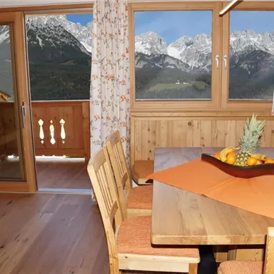 Ein gemütlicher Essbereich mit einem Holztisch und Stühlen. Durch die Fenster ist ein wunderschöner Blick auf die Berge zu sehen.