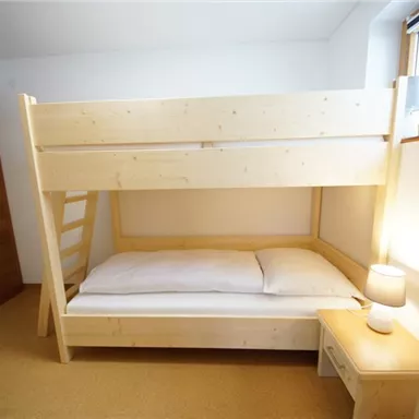 Ein gemütliches Schlafzimmer mit einem Kinderhochbett aus hellem Holz. Neben dem Bett steht ein Nachttisch mit einer kleinen Lampe.