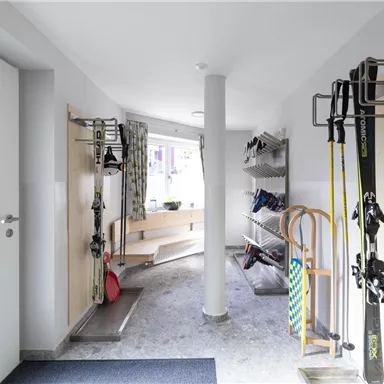 Ein moderner Eingangsbereich mit Ski- und Sportausrüstung. Der Raum ist hell und freundlich gestaltet, mit Platz für Schuhe und Jacken.
