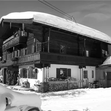 A traditional chalet in the snow with a large, sheltered roof. The wooden facade and balconies give the building a rustic charm.