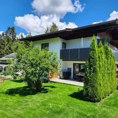 Ein modernes Haus mit einem schönen Garten und grünem Rasen. Es gibt Bäume und Sträucher im Freien, umgeben von einer malerischen Landschaft.