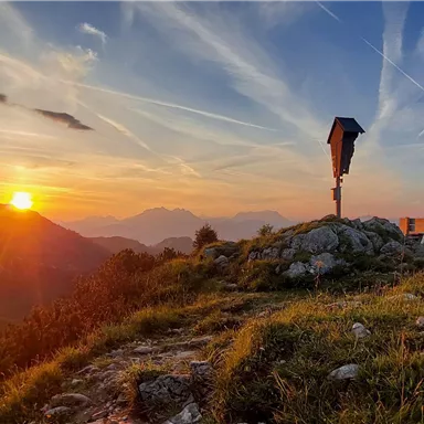 A beautiful sunset over the mountains with colorful clouds in the sky. In the foreground, green meadows and rocks are visible.