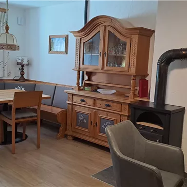 A cozy dining area with a wooden table and chairs. In the background, there is a traditional china cabinet and a stove.