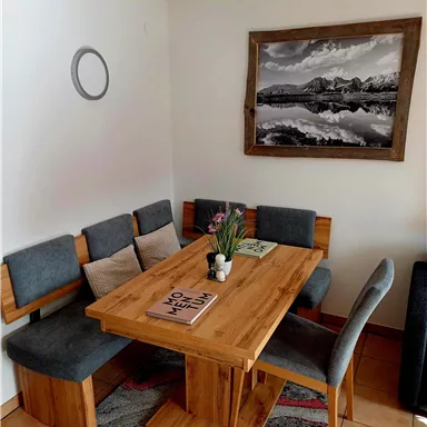 Ein gemütlicher Essbereich mit einem Holztisch und gepolsterten Stühlen. An der Wand hängt ein schwarz-weißes Bild einer Landschaft.