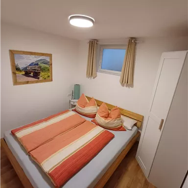 Ein gemütliches Schlafzimmer mit einem großen Bett und farbenfrohen Kissen. An der Wand hängt ein Bild und es gibt einen Schreibtisch mit einer Lampe.