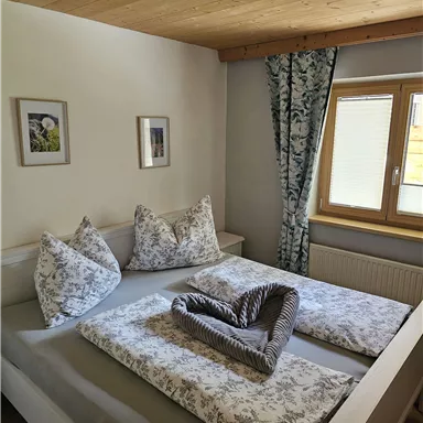 Ein gemütliches Schlafzimmer mit einem großen Bett und dekorativen Kopfkissen. Helle Wände und ein Fenster lassen viel Licht hereinhinein.