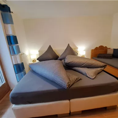 A cozy bedroom with a large bed and extra pillows. The walls are light and the room is friendly and inviting.