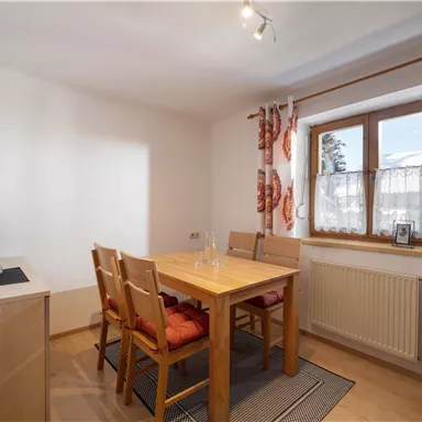 A bright dining room with a wooden chair and a table. The window lets in plenty of light and is decorated with colorful curtains.