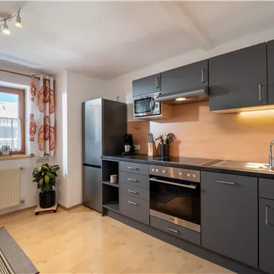 A modern kitchen with gray cabinets and a light wood countertop. Windows with curtains provide plenty of daylight.