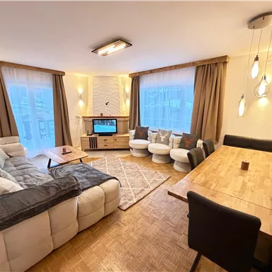 A modern living room with a comfortable couch, a table, and a television. Large windows provide plenty of natural light.